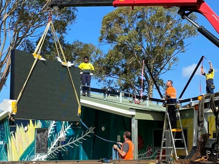 Crane lifting a new LED scoreboard onto a clubroom roof